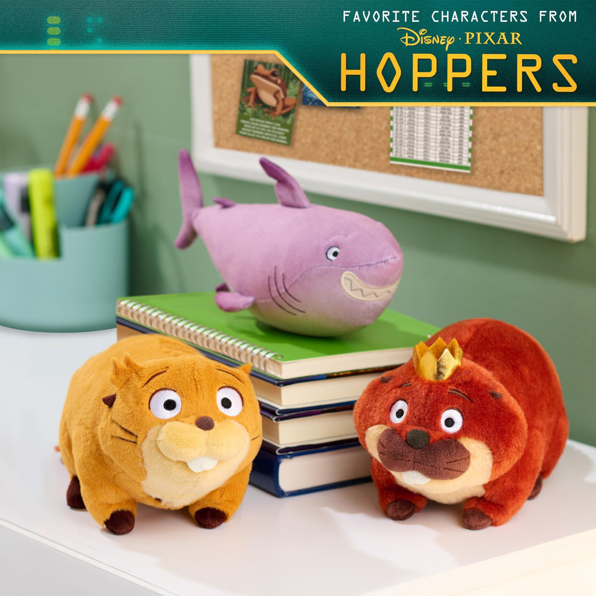 Three plush toys of animated animal characters on a desk with books and stationery in the background