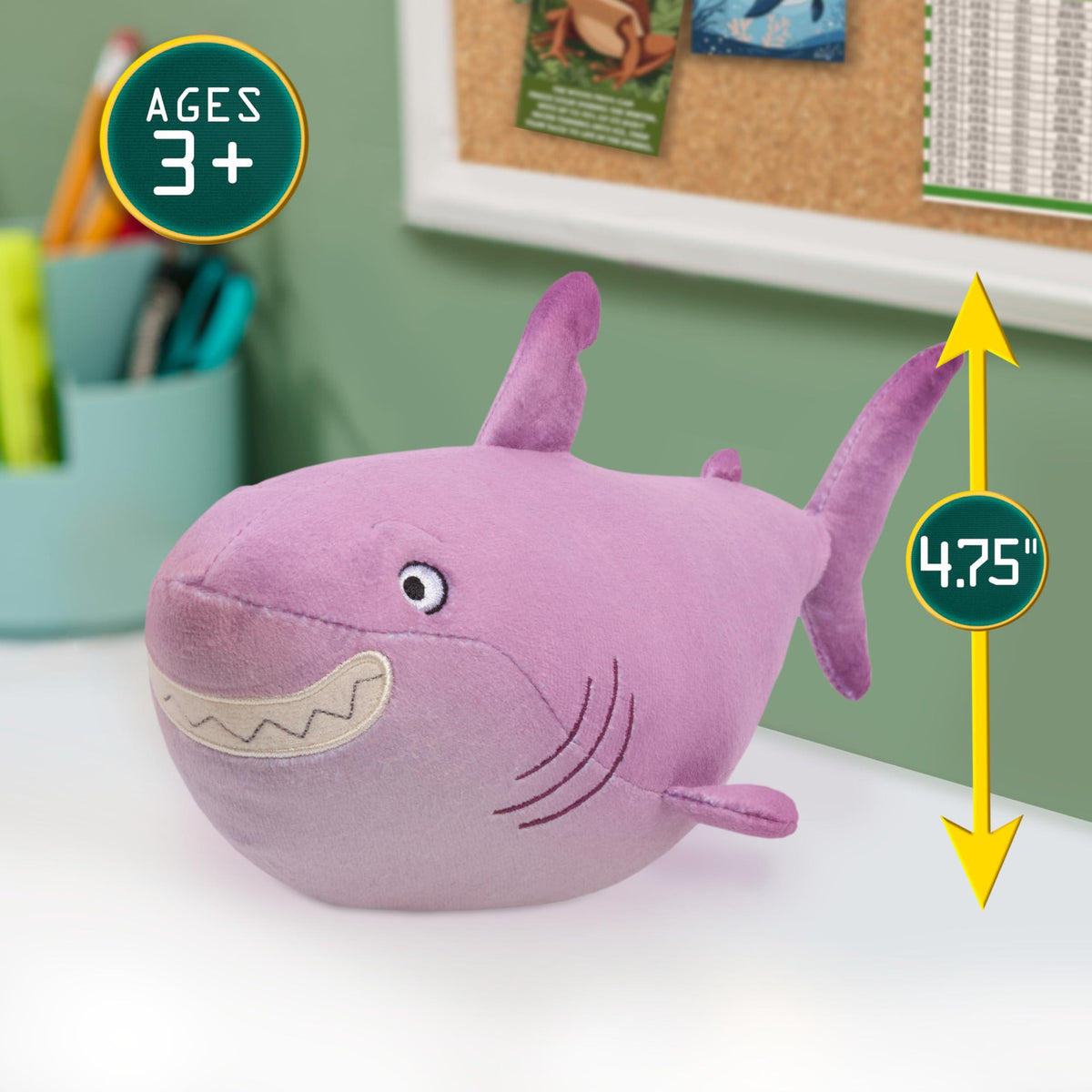 Plush purple shark toy with embroidered eyes and fins on a white surface against a blurred green background