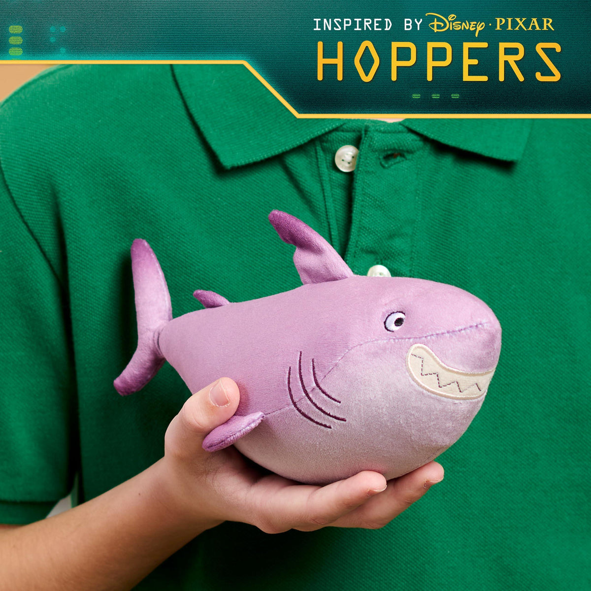 Child wearing green shirt holding a purple plush shark toy with a smiling face against dark background.