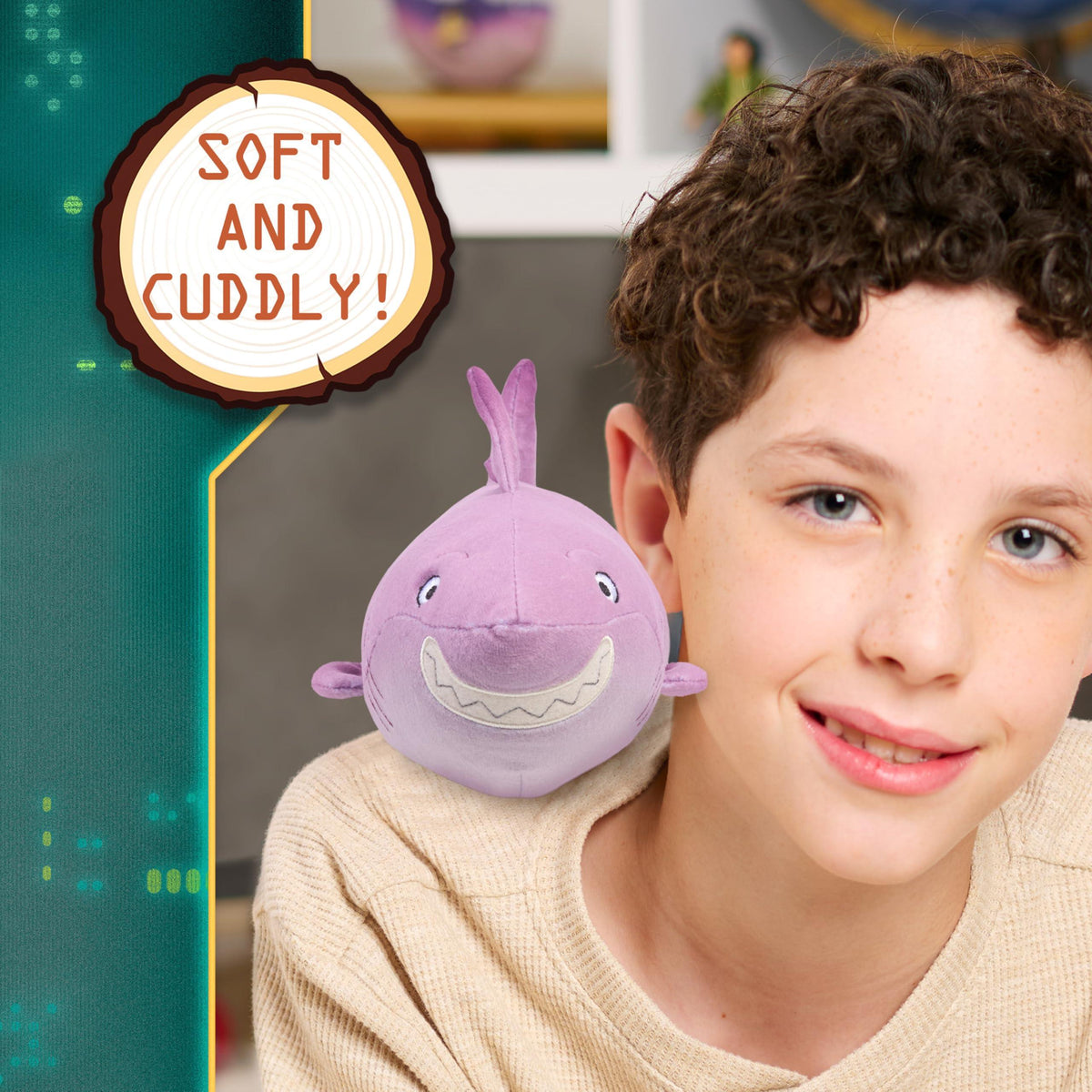 Young boy smiling with a purple plush shark toy on his shoulder and a "Soft and Cuddly" sign in the background.